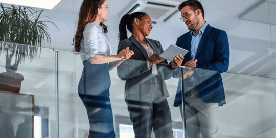 group of 3 professionals , 1 male, 2 female standing over a glass railing discussing health and safety in the office.