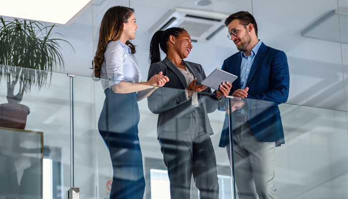 group of 3 professionals , 1 male, 2 female standing over a glass railing discussing health and safety in the office.