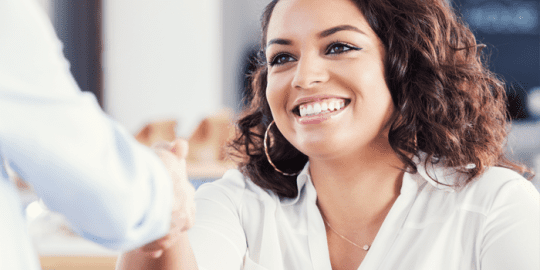 professional smiling woman sitting shaking the hand of one who has given a retail employment opportunity