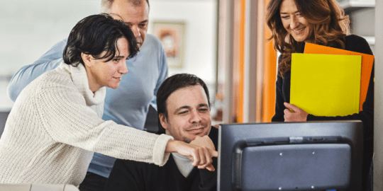 group of young professionals around a desktop computer reviewing social media checks