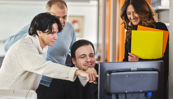 group of young professionals around a desktop computer reviewing social media checks