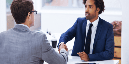 2 professionals sitting across from each other shaking hands after passing a background check in Canada to gain the job