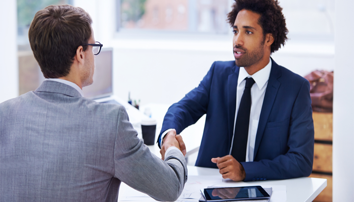 2 professionals sitting across from each other shaking hands after passing a background check in Canada to gain the job